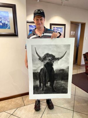 Man holding a framed charcoal drawing of a Highland cow inside an office.